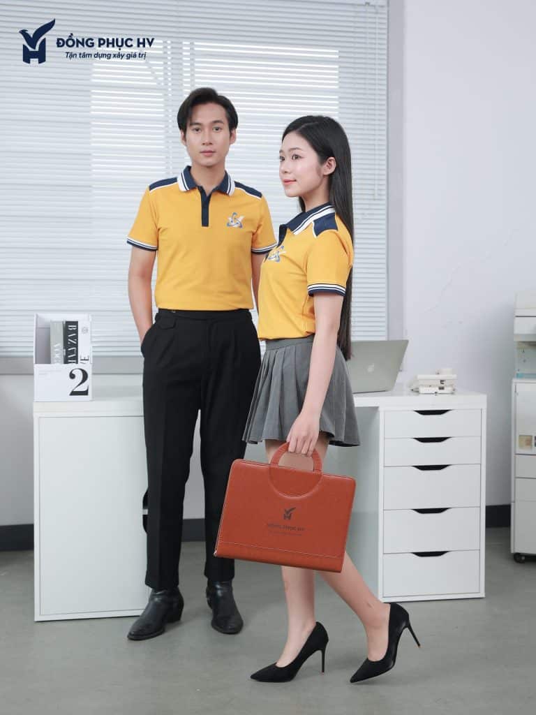 Nam nữ mặc polo vàng phối cổ xanh than, đứng cạnh bàn văn phòng